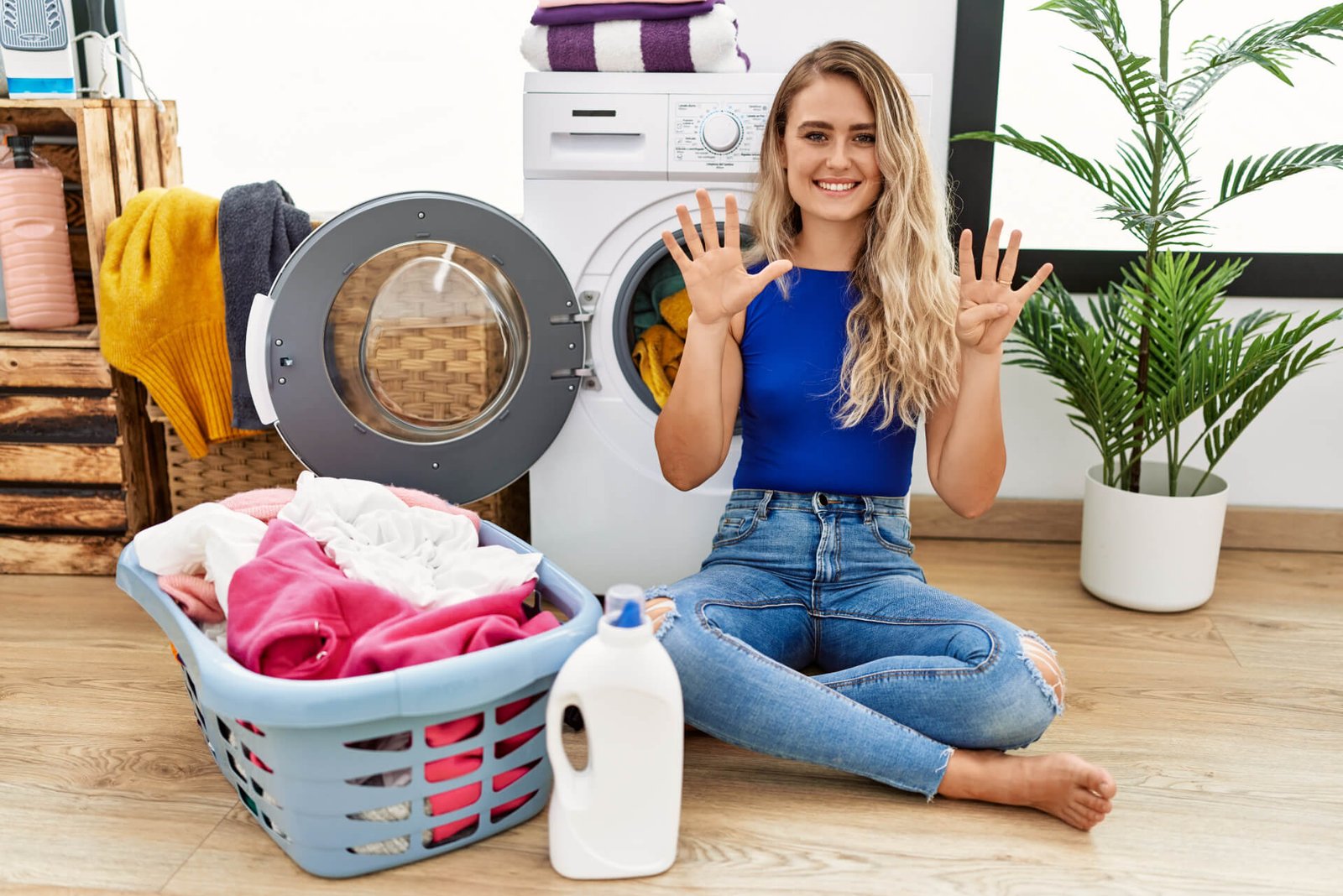 Chica rubia sentada mostrando que detergente usar para cuidar la lavadora